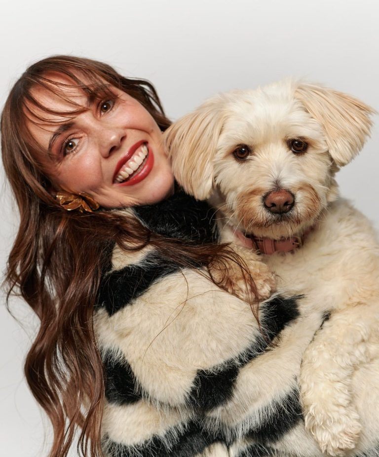 Helena Grossmann Frau mit lockigem, braunem Haar umarmt einen Hund mit hellbeigem Fell.